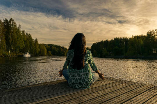 Today's Inspiration: December 21, 2022 woman, seen from the back, sitting in a lotus pose on a dock by a lake